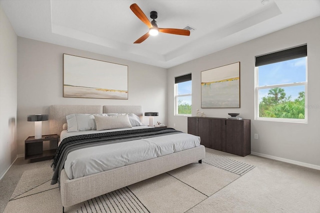 bedroom with light colored carpet, a raised ceiling, and ceiling fan