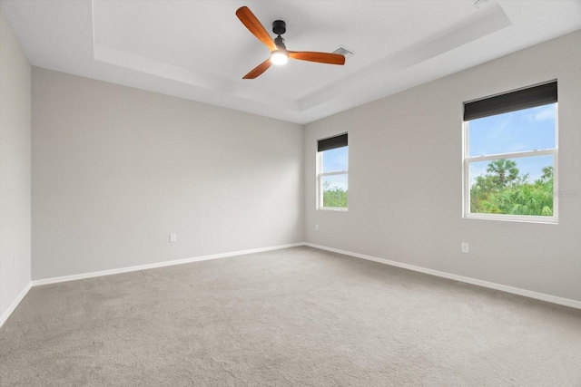 carpeted spare room with a raised ceiling and ceiling fan