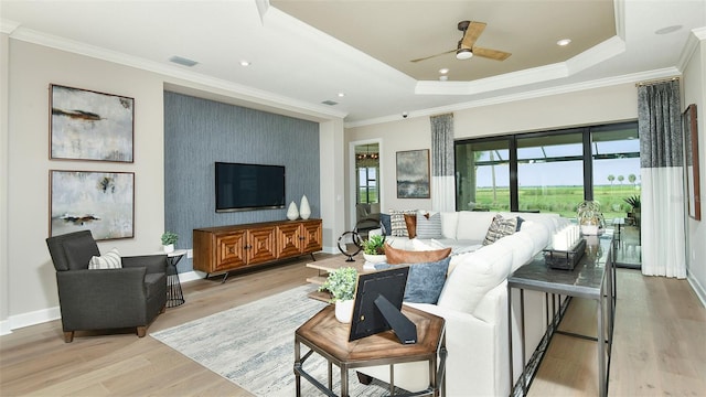 living room featuring ceiling fan, crown molding, a raised ceiling, and light wood-type flooring