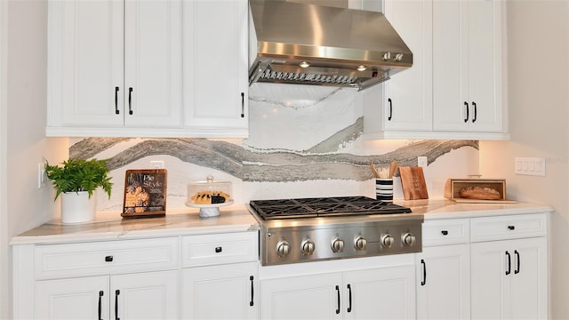 kitchen featuring backsplash, stainless steel gas stovetop, white cabinetry, light stone countertops, and ventilation hood