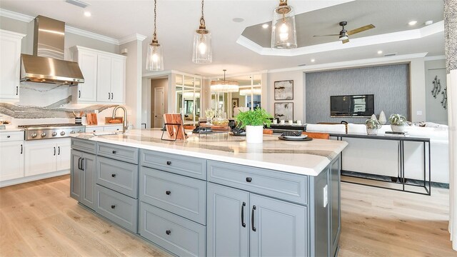 kitchen featuring decorative light fixtures, ceiling fan, stainless steel gas cooktop, white cabinets, and wall chimney exhaust hood