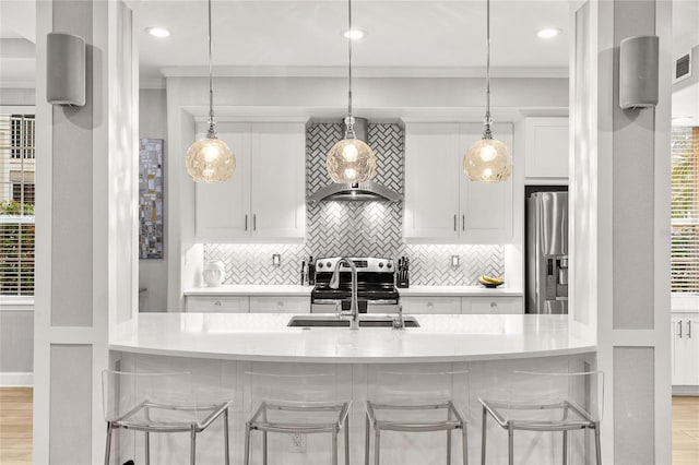 kitchen featuring wall chimney exhaust hood, white cabinetry, stainless steel appliances, crown molding, and a breakfast bar area