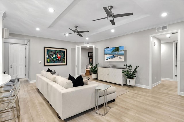 living room featuring a tray ceiling, ornamental molding, and light wood-type flooring