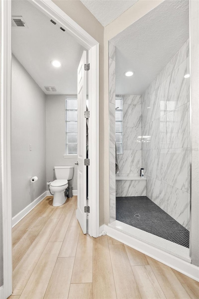 bathroom featuring a tile shower, toilet, and a textured ceiling