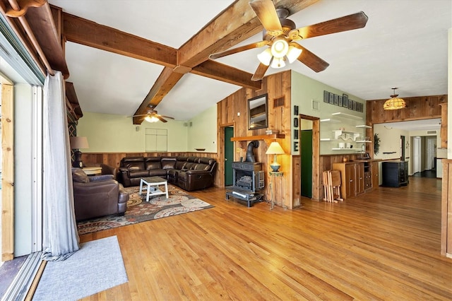 living room featuring hardwood / wood-style floors, wood walls, a wood stove, vaulted ceiling with beams, and ceiling fan