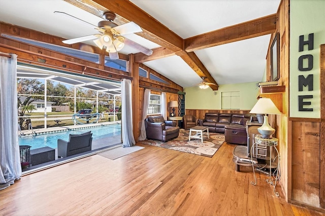 living room featuring vaulted ceiling with beams, hardwood / wood-style floors, ceiling fan, and wood walls