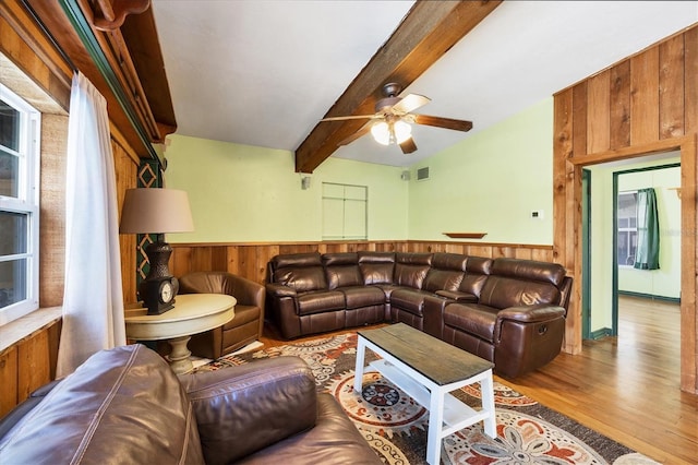 living room with light hardwood / wood-style flooring, ceiling fan, wooden walls, and beamed ceiling