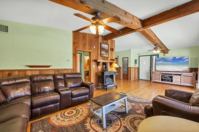 living room featuring a wood stove, wooden walls, ceiling fan, beam ceiling, and light hardwood / wood-style floors