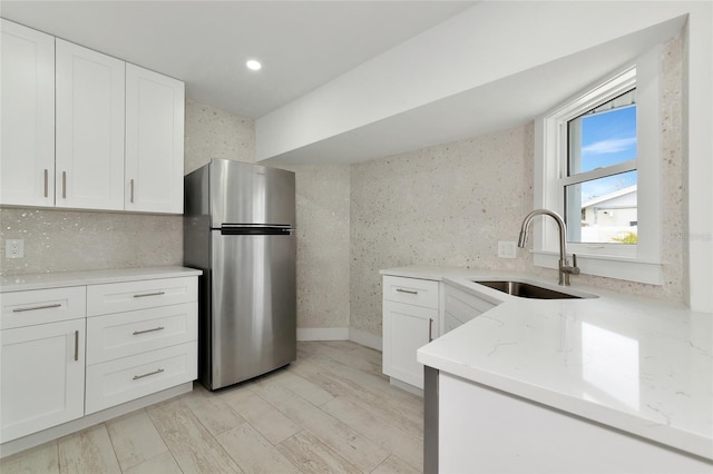 kitchen featuring sink, white cabinetry, tasteful backsplash, light stone counters, and stainless steel refrigerator