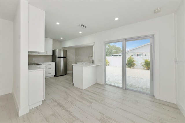 kitchen featuring stainless steel refrigerator, tasteful backsplash, sink, white cabinets, and kitchen peninsula