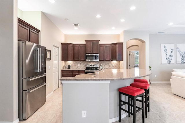 kitchen with appliances with stainless steel finishes, tasteful backsplash, dark brown cabinetry, and a breakfast bar area