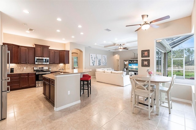 kitchen with an island with sink, stainless steel appliances, dark brown cabinetry, backsplash, and a breakfast bar area