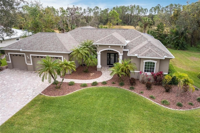 view of front facade with stucco siding, a front yard, decorative driveway, and a garage