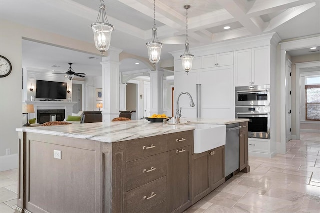 kitchen with a kitchen island with sink, a sink, white cabinetry, stainless steel appliances, and ornate columns