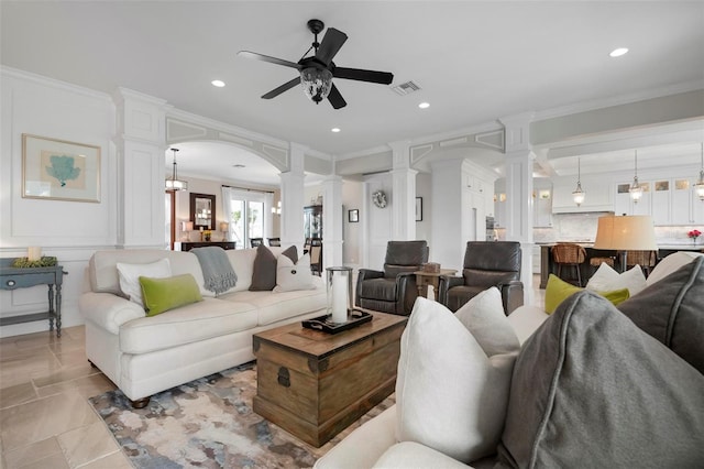 living room featuring a ceiling fan, visible vents, decorative columns, arched walkways, and crown molding