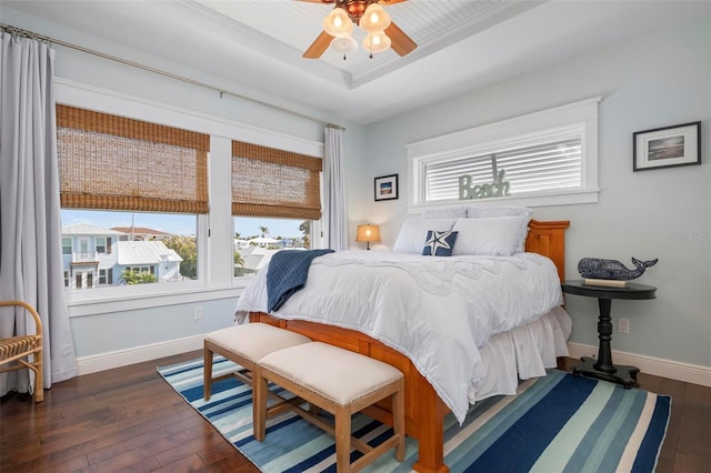 bedroom featuring multiple windows, a raised ceiling, baseboards, and wood-type flooring