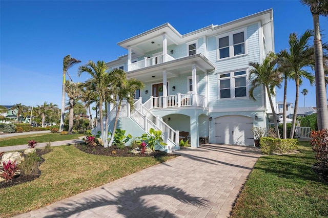 beach home featuring decorative driveway, a porch, a front yard, a balcony, and stairs