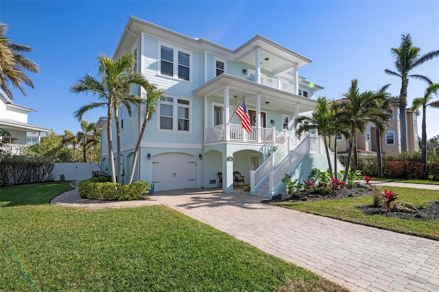 coastal home with a front lawn, stairs, covered porch, decorative driveway, and a balcony