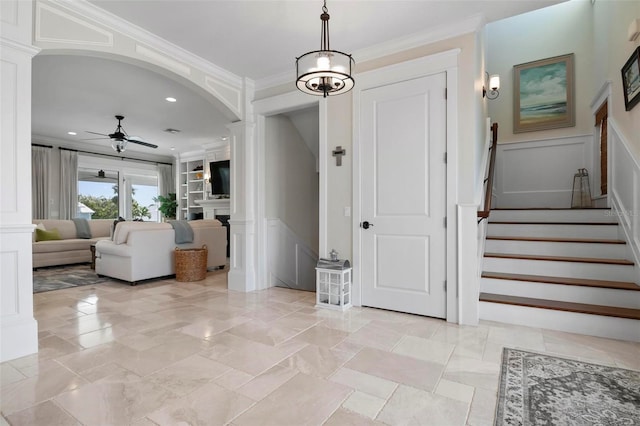 entryway featuring ornamental molding, a ceiling fan, arched walkways, a decorative wall, and stairs