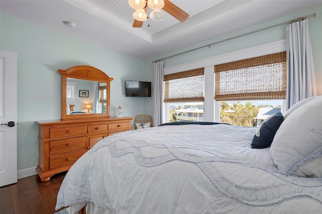 bedroom with a ceiling fan, a raised ceiling, baseboards, and dark wood-style flooring