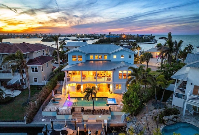 rear view of house with a balcony, an outdoor pool, a water view, a patio area, and metal roof