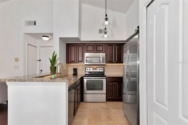 kitchen featuring decorative backsplash, hanging light fixtures, light stone counters, kitchen peninsula, and stainless steel appliances