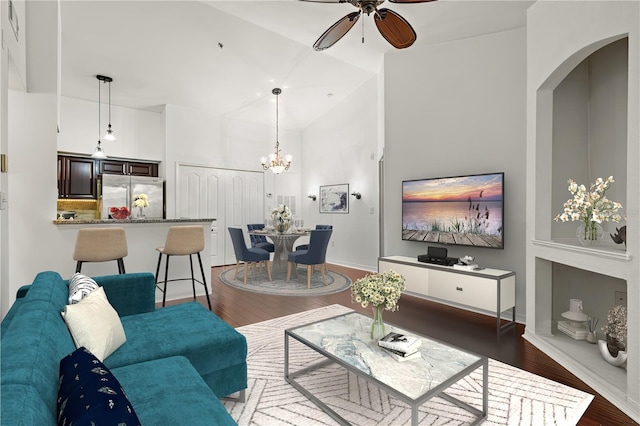 living room with ceiling fan with notable chandelier, high vaulted ceiling, and dark hardwood / wood-style floors