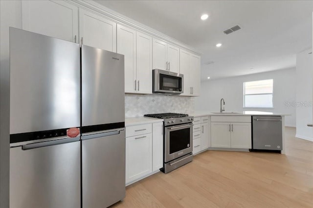 kitchen with white cabinetry, light hardwood / wood-style floors, stainless steel appliances, tasteful backsplash, and sink