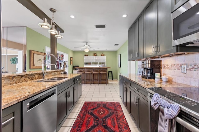 kitchen featuring light stone counters, visible vents, a sink, appliances with stainless steel finishes, and tasteful backsplash