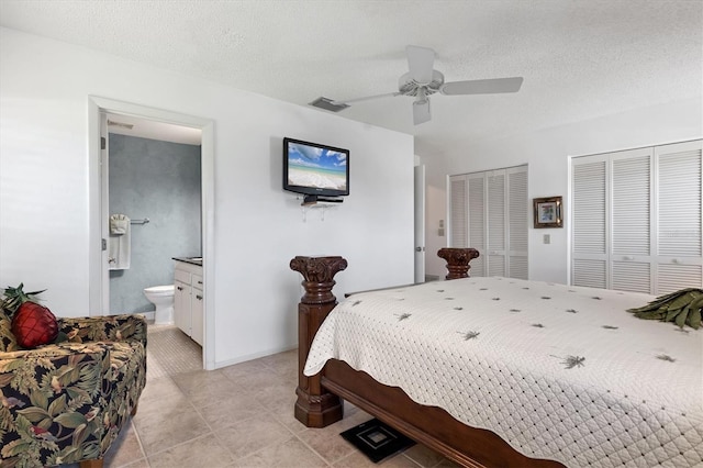 bedroom featuring visible vents, connected bathroom, multiple closets, a textured ceiling, and a ceiling fan