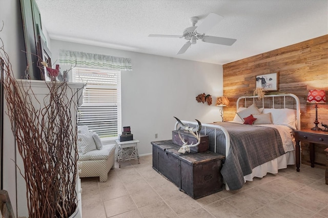 bedroom featuring ceiling fan, wooden walls, light tile patterned floors, and a textured ceiling