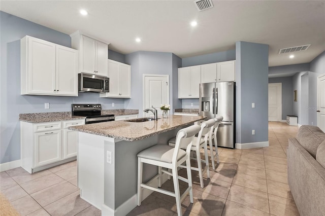 kitchen with a center island with sink, stainless steel appliances, visible vents, open floor plan, and white cabinetry