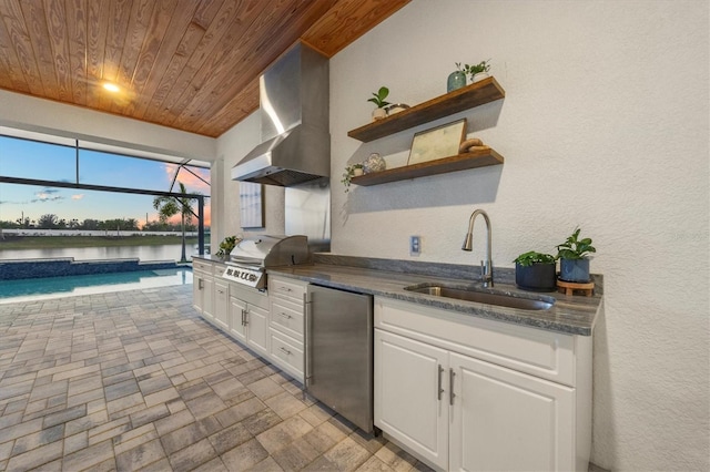 kitchen featuring wooden ceiling, white cabinetry, sink, wall chimney exhaust hood, and stainless steel fridge