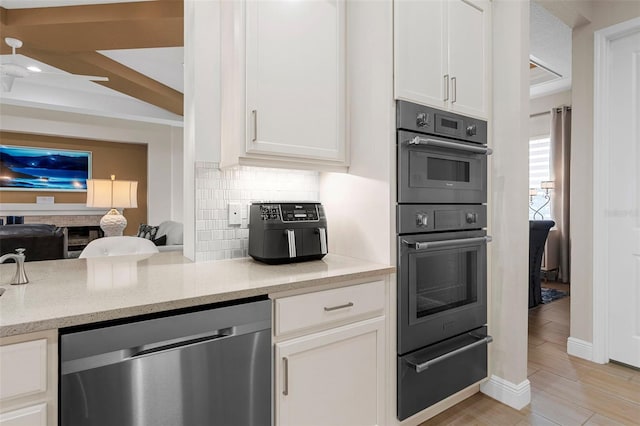 kitchen with multiple ovens, light stone counters, white cabinets, decorative backsplash, and stainless steel dishwasher