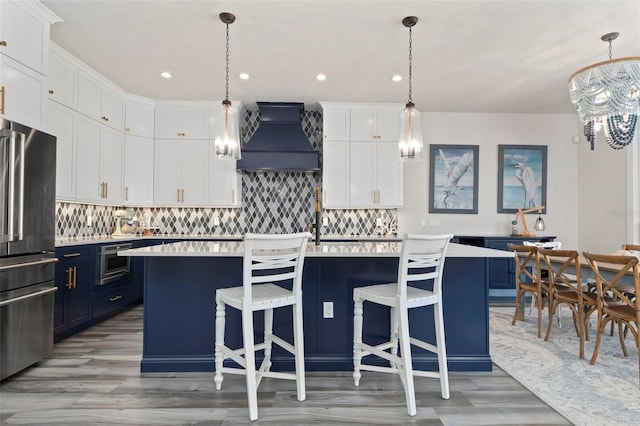 915 N Shore Dr, Anna Maria, FL 34216 - kitchen with an inviting chandelier, light wood-style floors, blue cabinetry, freestanding refrigerator, and custom exhaust hood