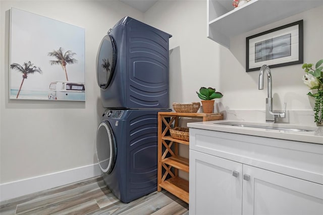 915 N Shore Dr, Anna Maria, FL 34216 - laundry area featuring stacked washer and clothes dryer, baseboards, cabinet space, a sink, and light wood finished floors