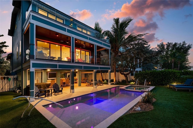 915 N Shore Dr, Anna Maria, FL 34216 - back of property at dusk featuring a lawn, a pool with connected hot tub, fence, a balcony, and a patio