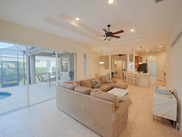 tiled living room with ceiling fan and a tray ceiling