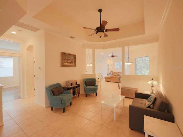 living room featuring ceiling fan, a raised ceiling, crown molding, and light tile patterned flooring