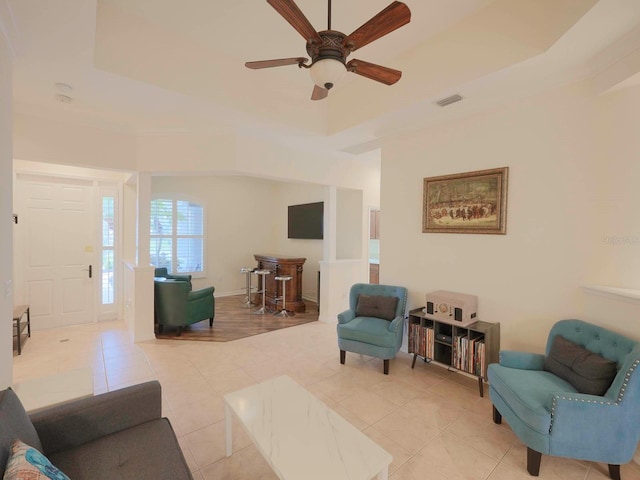 living room featuring ceiling fan, light tile patterned flooring, and a tray ceiling