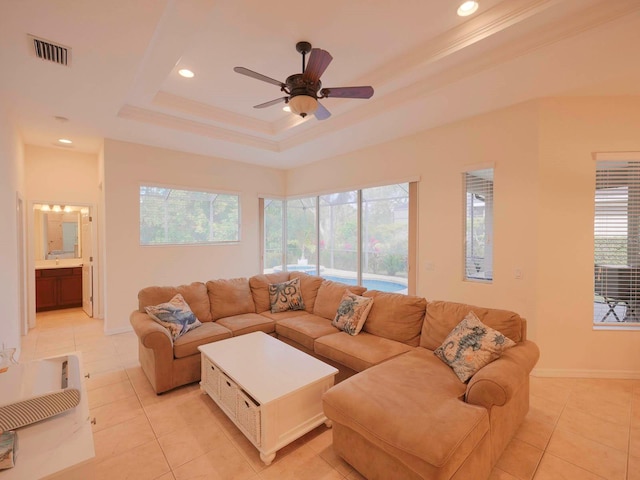 tiled living room with ceiling fan, a tray ceiling, and crown molding