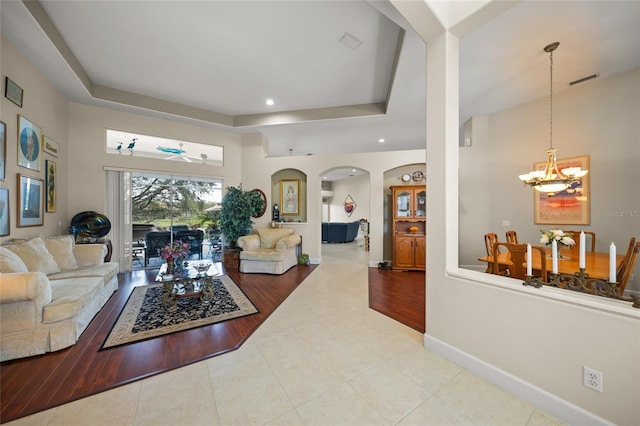 living room featuring a raised ceiling, light tile patterned floors, and a notable chandelier