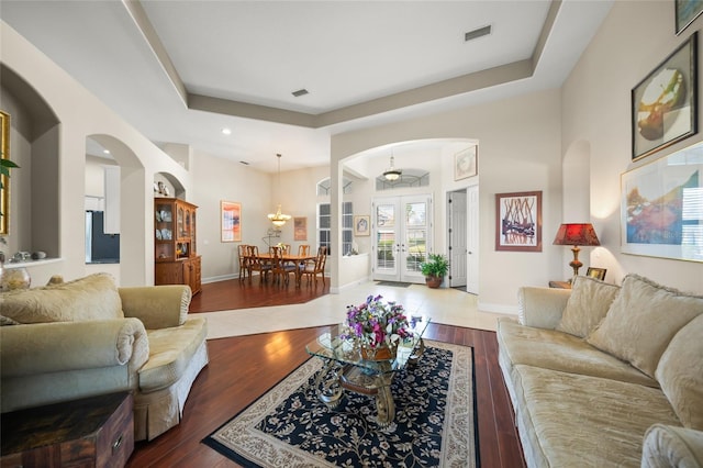 living room with hardwood / wood-style floors, a tray ceiling, french doors, and an inviting chandelier