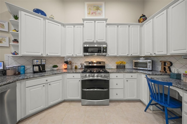 kitchen with white cabinets, stainless steel appliances, dark stone counters, backsplash, and light tile patterned floors