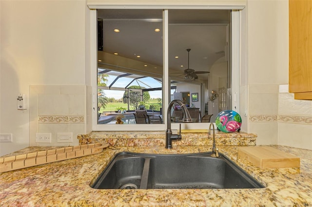 kitchen with light stone counters, a sink, a sunroom, and a ceiling fan