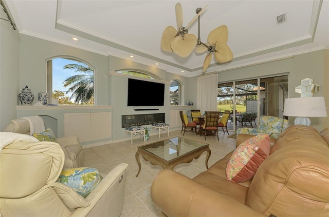 living room with a tray ceiling, crown molding, light tile patterned floors, visible vents, and ceiling fan