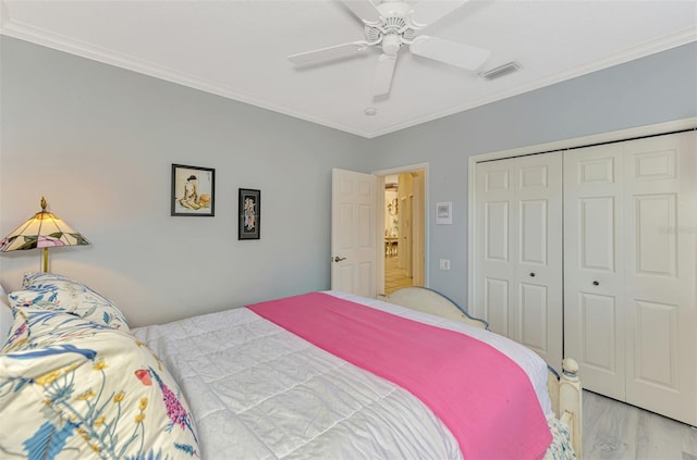 bedroom with a closet, visible vents, ornamental molding, ceiling fan, and wood finished floors