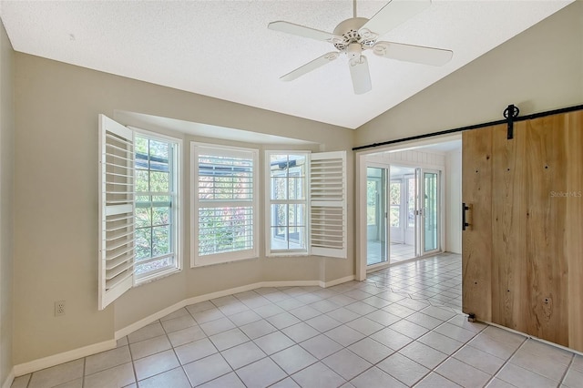 tiled spare room featuring lofted ceiling, a barn door, ceiling fan, and a textured ceiling