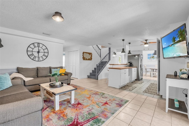 living room with ceiling fan, light tile patterned flooring, and a textured ceiling