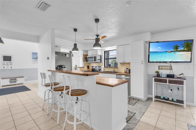 kitchen featuring light tile patterned floors, wooden counters, white cabinetry, and stainless steel appliances